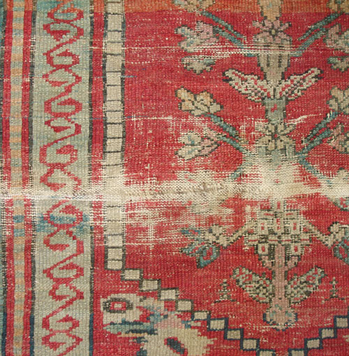 An antique Turkish rug with large worn areas before repair.