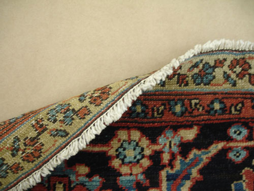 An antique Persian rug with unravelling fringe after repair.